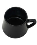 Black porcelain coffee mug from the 12-piece coffee and tea set with metal stand, placed on a floor chair.